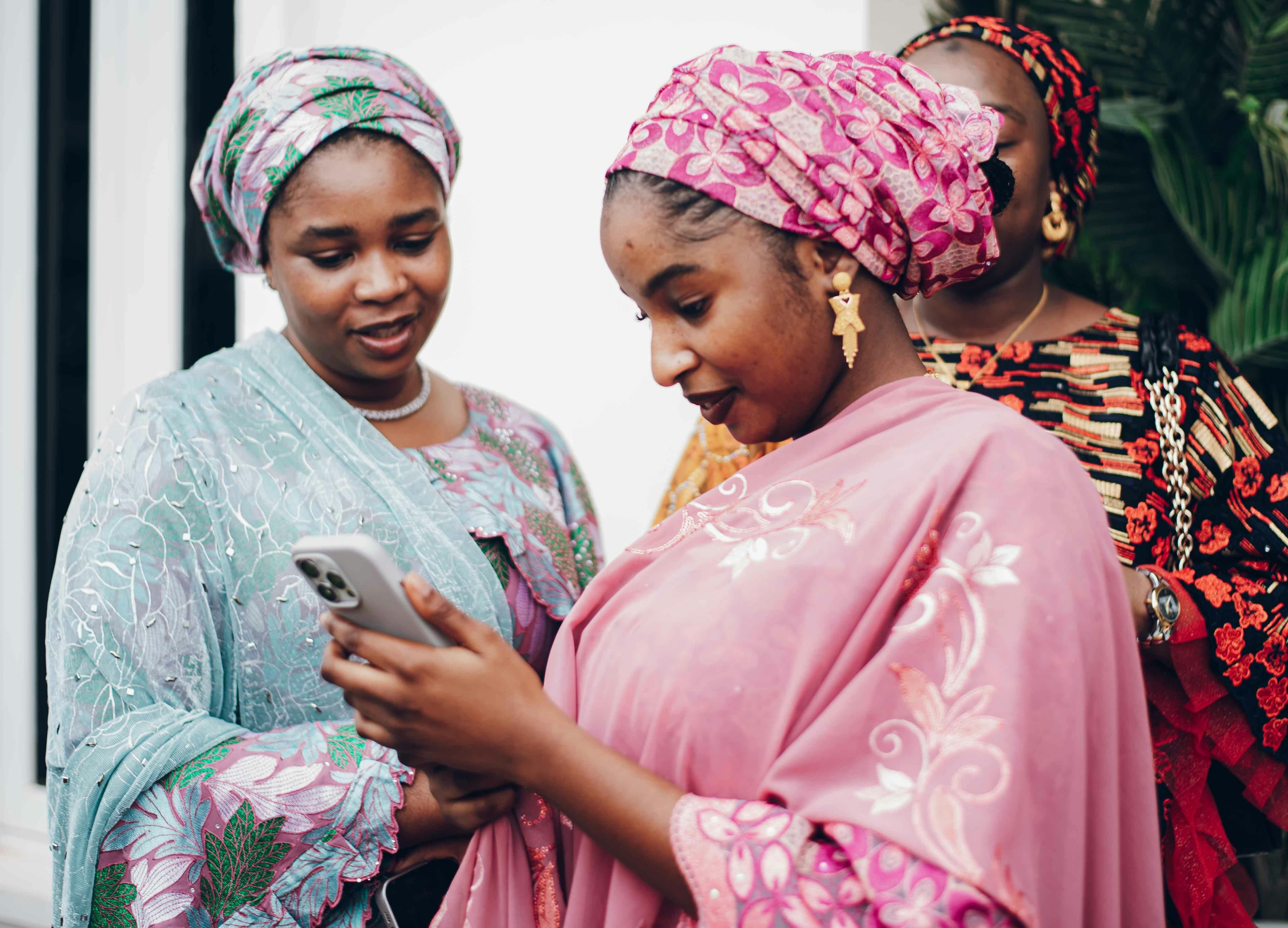 Duas mulheres com roupas tradicionais a olhar juntas para um iPhone
