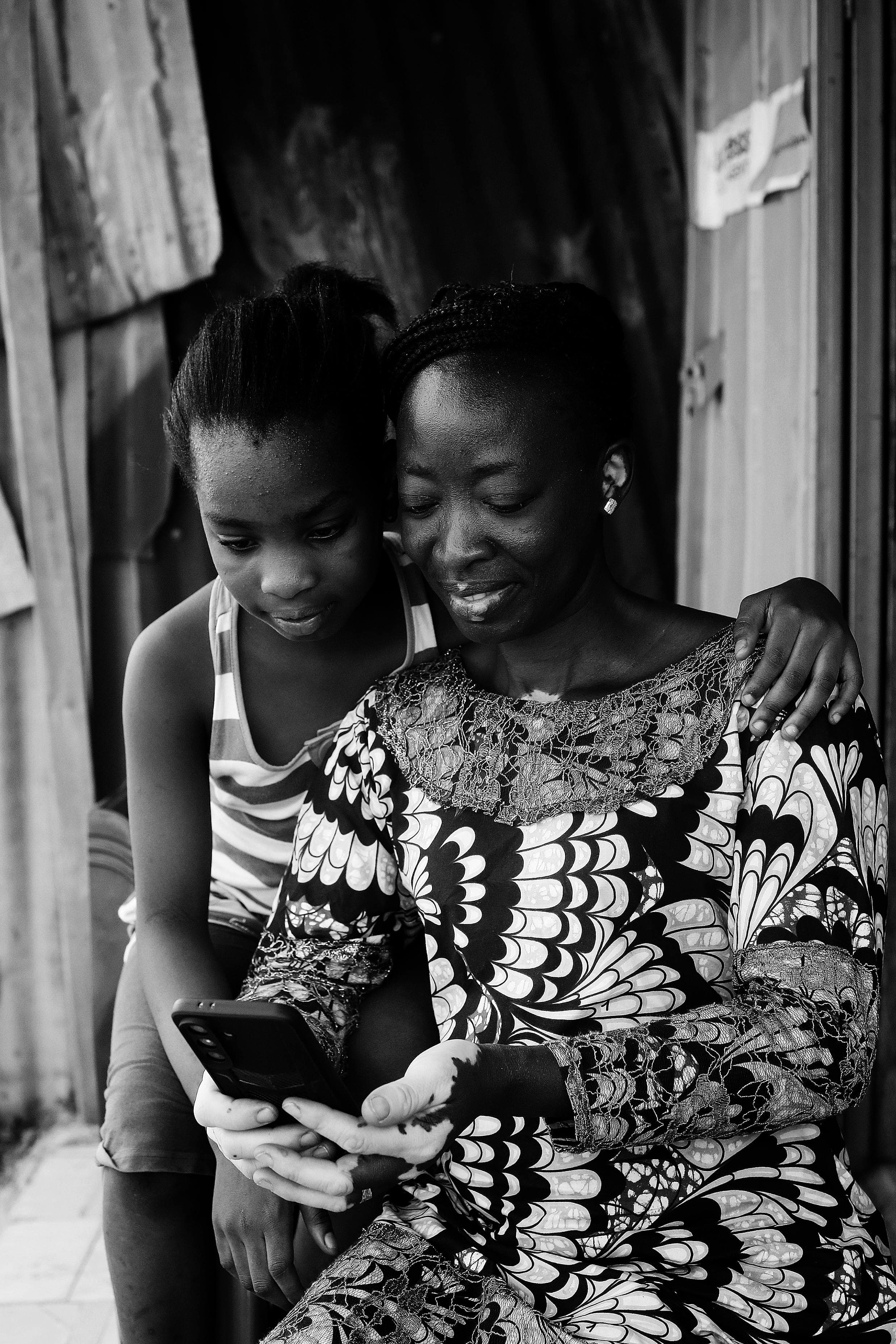 Frau und Mädchen schauen gemeinsam auf ein Telefon vor einem Haus